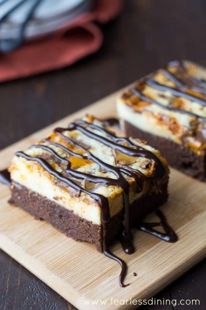 These delicious gluten-free Cheesecake Brownie Bars are so hard to resist. Chocolaty moist brownie topped with creamy cheesecake, chopped Butterfinger candy, and fudge. 